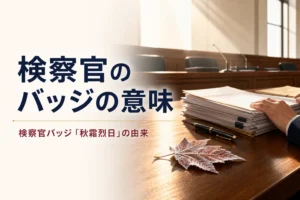 検察官のバッジ「秋霜烈日」の意味と由来を紹介する記事のアイキャッチ。日差しの差し込む法廷の机と書類